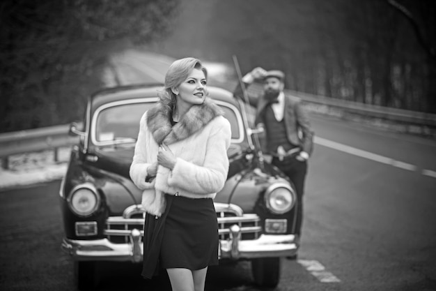 Couple amoureux à un rendez-vous romantique Voiture de collection rétro et réparation automobile par chauffeur mécanicien Voyage et voyage d'affaires ou auto-stop Escorte d'une fille par la sécurité Homme barbu et femme sexy en manteau de fourrure