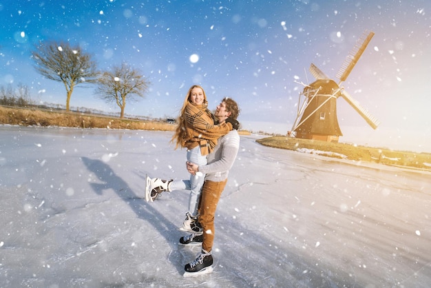 Couple d'amoureux s'amusant sur la glace dans un paysage typiquement hollandais avec moulin à vent femme et homme patin à glace