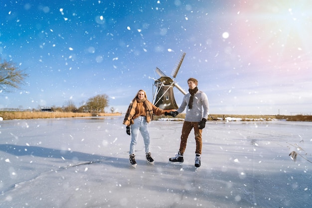 Couple d'amoureux s'amusant sur la glace dans un paysage typiquement hollandais avec moulin à vent femme et homme patin à glace