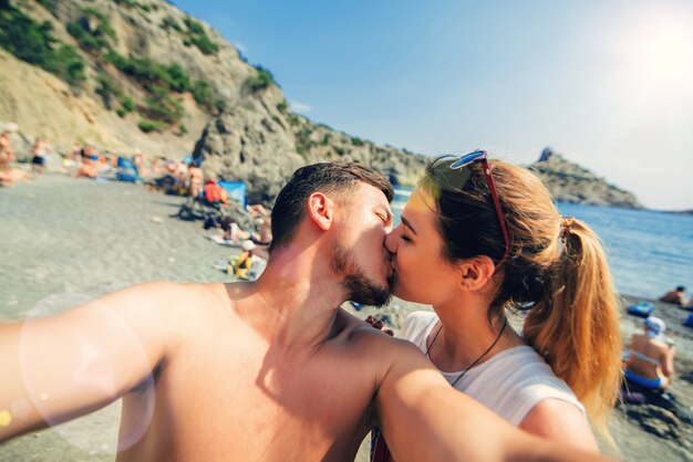 Couple d'amoureux s'embrassant et prenant des selfies au téléphone sur la plage