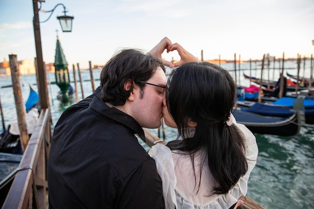 Un couple d'amoureux s'embrasse à Venise pendant le coucher du soleil et ils font un cœur avec leurs mains un moment romantique
