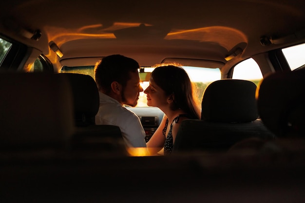 Couple amoureux s'embrasser assis dans la voiture au coucher du soleil