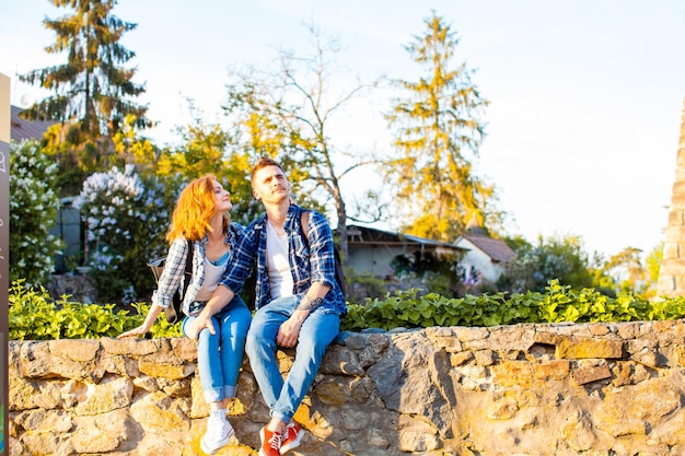 Un couple d'amoureux avec des sacs à dos est assis sur un mur de pierre