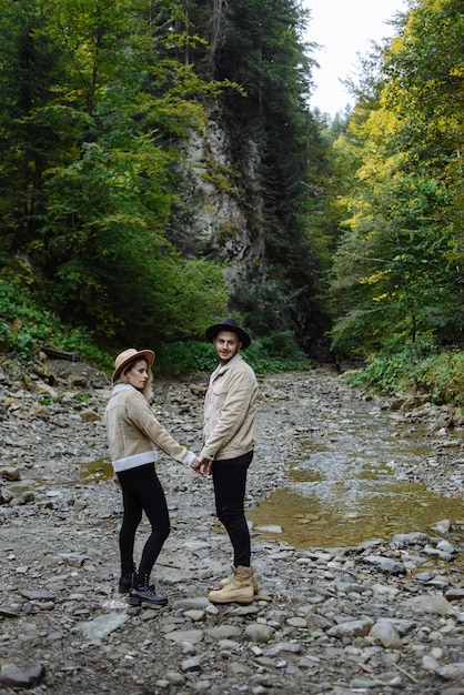 couple d'amoureux se promène le long d'un ruisseau de montagne tout en rédigeant les mains. Contexte d'aventure