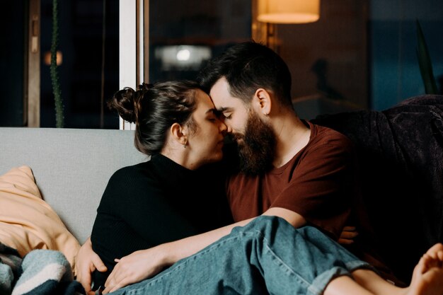 Un couple d'amoureux se regardant sur le canapé avec amour tout en touchant les visages avec copie espace