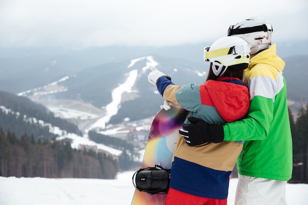 Couple d'amoureux snowboarders sur les pentes glaciale journée d'hiver pointant