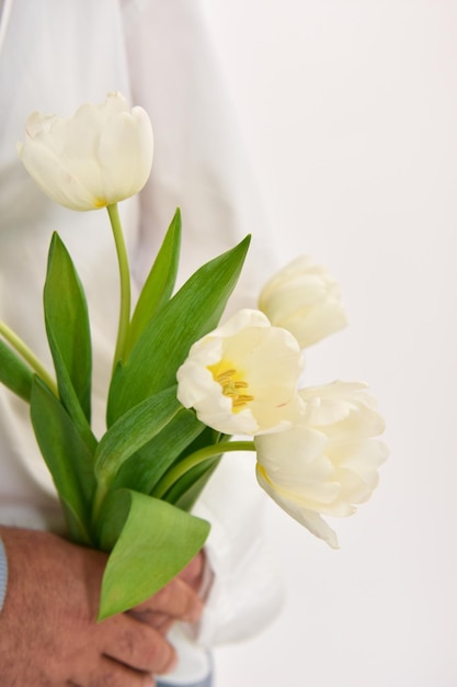 Couple d'amoureux tenant un bouquet de tulipes blanches sur fond blanc.