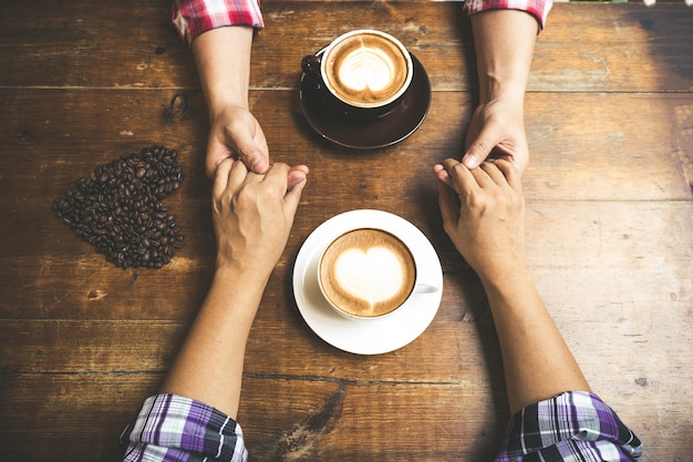 Photo couple amoureux tenant le café à la main sur la table en bois.