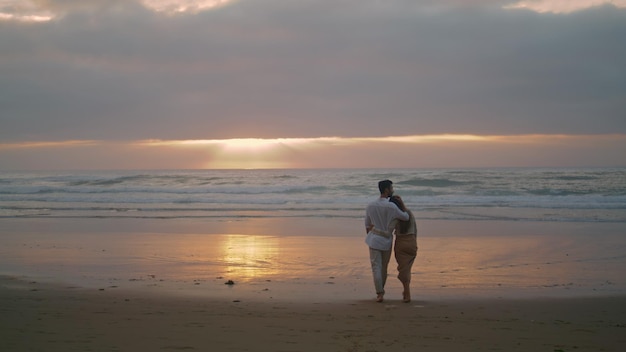 Un couple amoureux traversant le coucher de soleil au bord de la mer Des gens d'été embrassant la nature de la mer