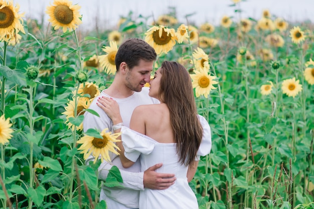 Couple d'amoureux en vêtements blancs posant dans un champ de tournesols