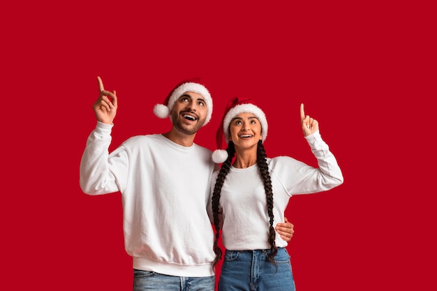 Photo couple arabe rêveur portant des chapeaux de père noël pointant vers le haut sur l'espace de copie