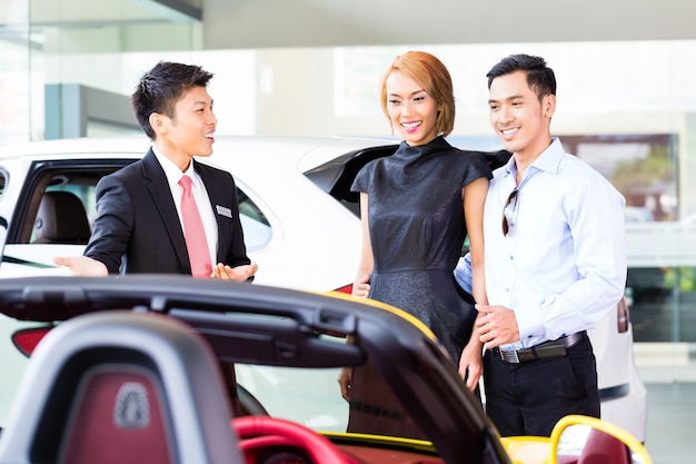 Couple asiatique achetant une voiture chez un concessionnaire automobile consultant le vendeur