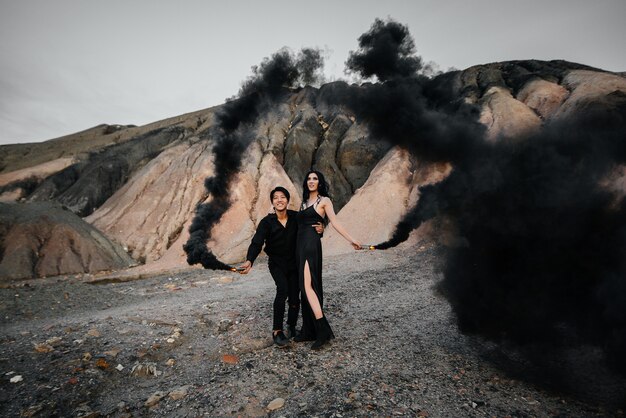 Photo un couple asiatique amoureux a allumé des bombes fumigènes noires dans les montagnes. fumée colorée