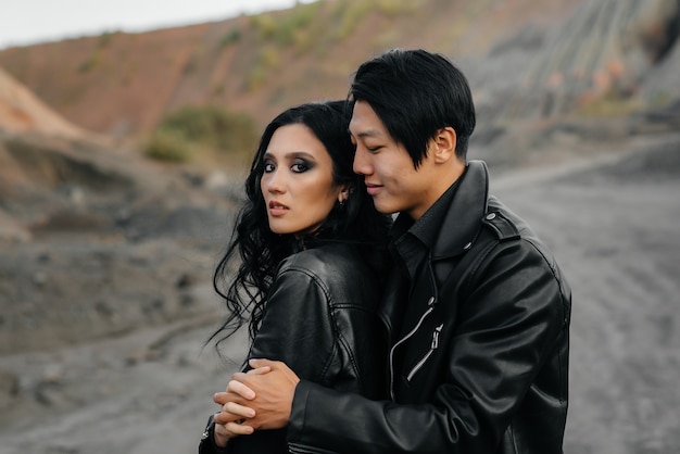 Un couple asiatique amoureux dans des vêtements en cuir noir se promène dans la nature parmi les arbres. Style, mode, amour