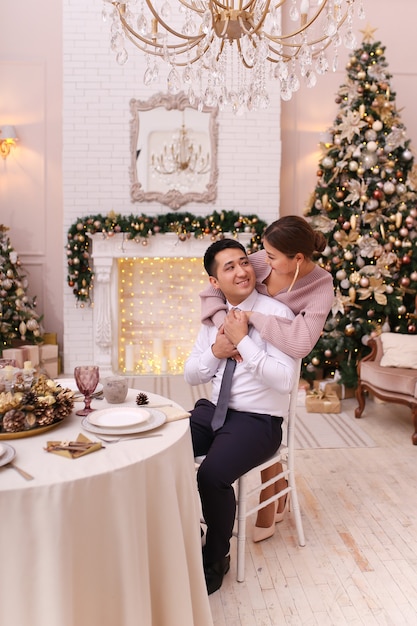 Couple asiatique amoureux homme et femme dans des tenues élégantes s'asseoir près d'une cheminée et d'un arbre, dîner de Noël