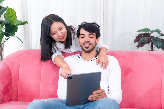 Couple asiatique assis sur un canapé avec une tablette pc célébrant une bonne affaire en ligne ou un succès commercial à la maison