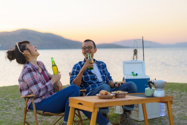 Couple asiatique buvant de la bière en bouteille dans leur zone de camping avec lac