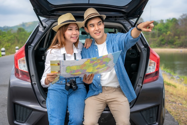 Couple asiatique avec une carte assise à l'arrière de la voiture