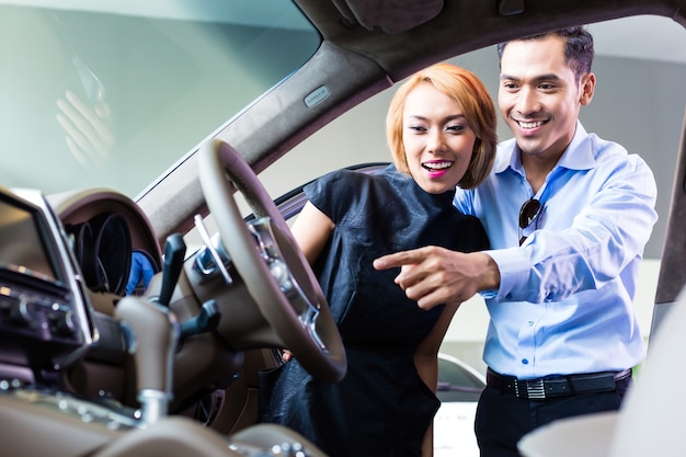 Photo couple asiatique choisissant une voiture de luxe chez un concessionnaire automobile à l'intérieur