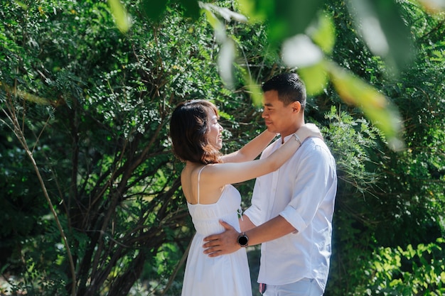 Couple asiatique passionné en vêtements blancs debout dans un buisson dans un parc, loin des yeux des autres. Se regarder, se tenir les uns les autres.