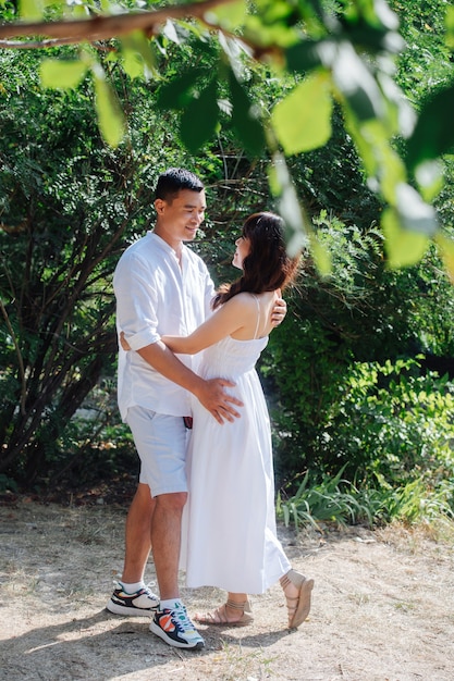 Couple asiatique romantique en vêtements blancs debout dans un buisson dans un parc, loin des yeux des autres. Se regarder, se tenir les uns les autres.