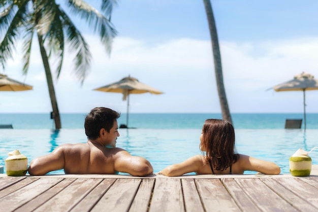 couple asiatique voyageur avec noix de coco se détendre dans un complexe hôtelier de luxe avec piscine à débordement avec plage de la mer