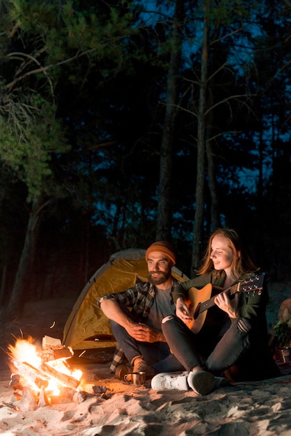 Photo couple assis et chantant près d'une tente la nuit