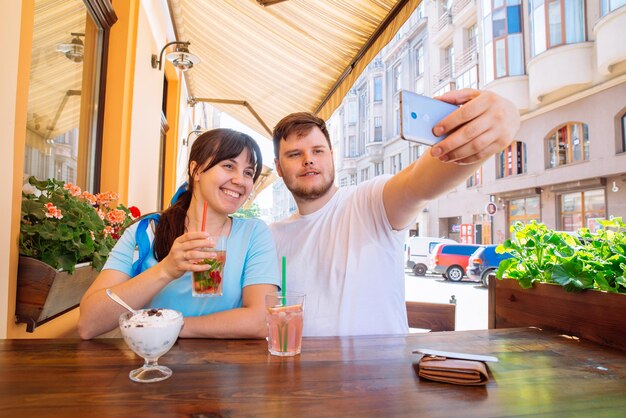 Couple assis dans un café en été en prenant des boissons fraîches selfie