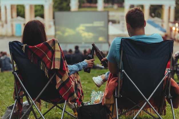 Couple assis dans des chaises de camping dans le parc de la ville regardant un film en plein air au cinéma en plein air