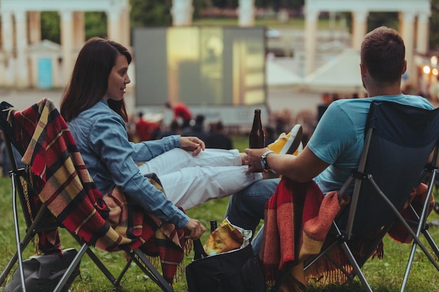 Couple assis dans des chaises de camping dans le parc de la ville regardant un film en plein air au cinéma en plein air