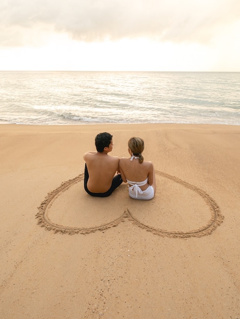 Couple assis dans le coeur s'appuyant sur la plage de sable se relaxant au soleil.