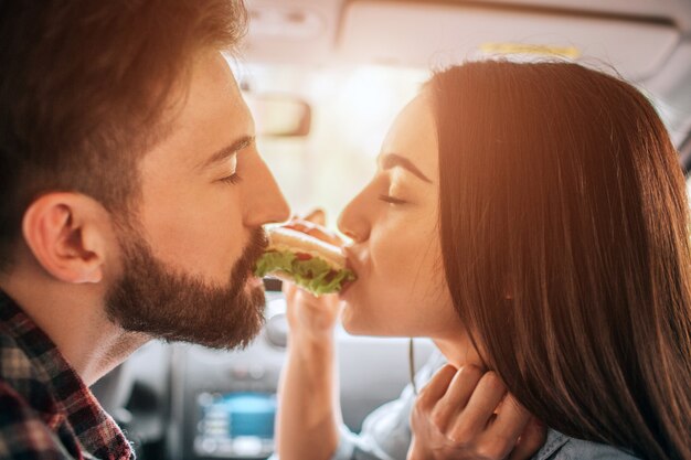 couple assis dans la voiture et manger un sandwich des deux côtés