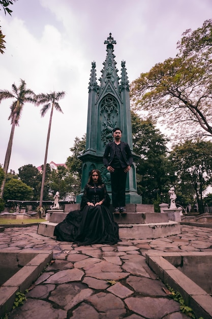 Un couple assis et debout devant un monument funéraire lors de la visite d'un ami décédé avec une expression triste