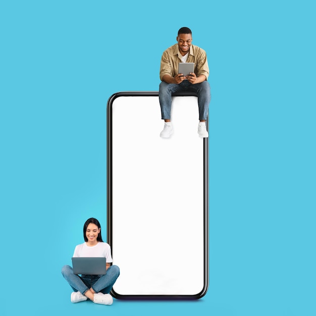 Couple assis sur un écran de smartphone blanc vide et utilisant des gadgets