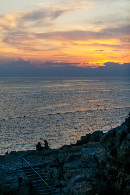 Couple assis sur une falaise rocheuse à la recherche d'un rendez-vous romantique au coucher du soleil