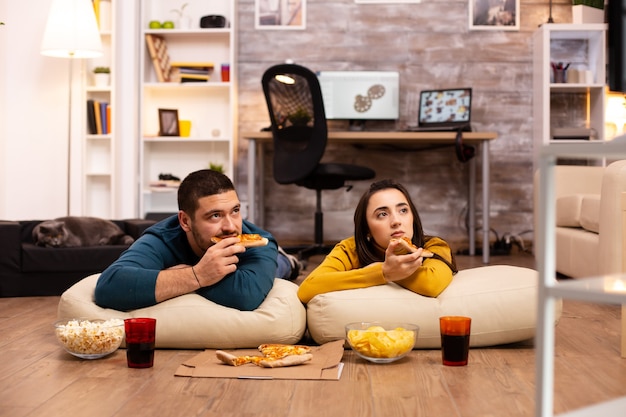 Couple assis par terre et regardant la télévision dans leur salon.