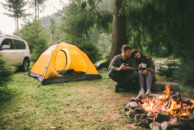 Couple assis près du feu et boire du thé chaud concept de randonnée