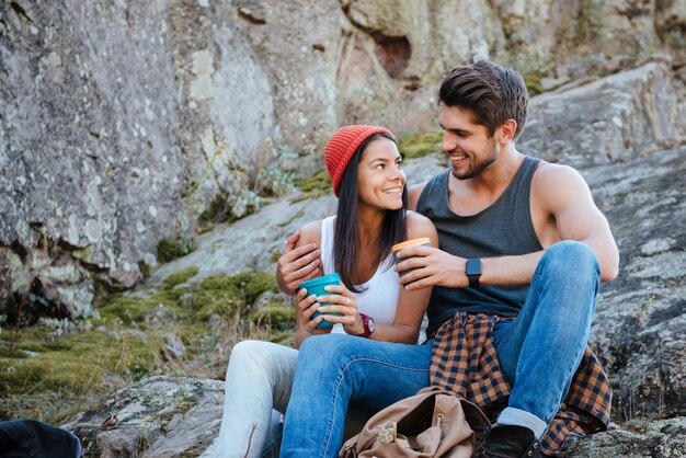 Couple assis sur un rocher avec des tasses de thé. les yeux dans les yeux