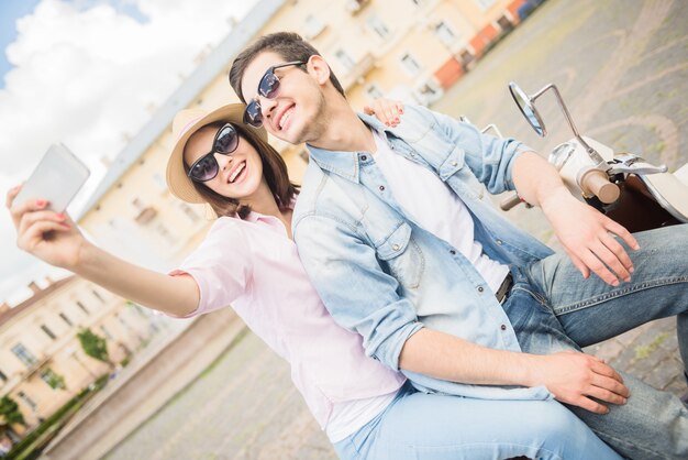 Couple assis sur un scooter et prenant selfie.