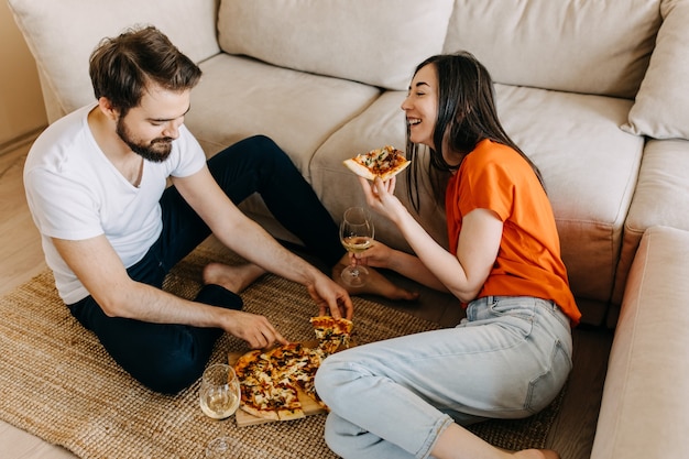 Couple assis sur le sol, manger de la pizza et boire du vin