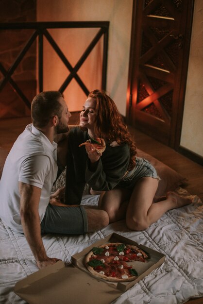 Couple assis sur le tapis et manger de la pizza