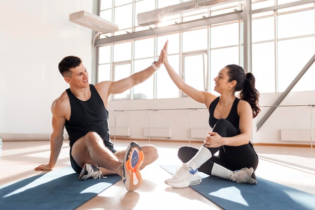 Un couple athlétique en tenue de sport salue dans la salle de sport une fille de fitness et un entraîneur donne cinq hauts