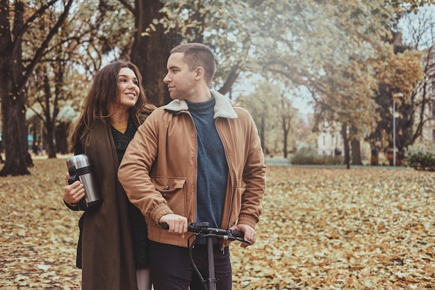 Un couple attrayant a une belle promenade romantique au parc d'automne avec un scooter.