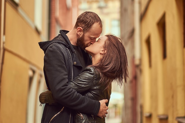 Photo couple attrayant, homme barbu et fille brune s'embrassant à l'extérieur de la vieille rue européenne sur un fond.