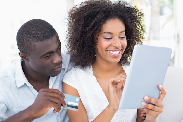 Couple attrayant avec tablette ensemble sur le canapé pour faire des achats en ligne