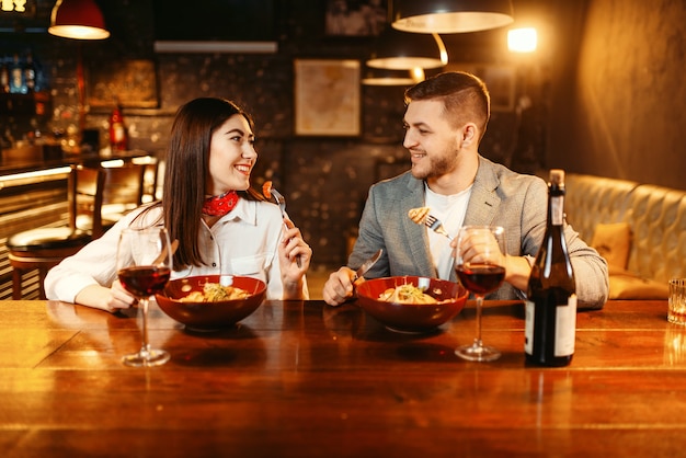 Couple au comptoir de bar en bois, dîner romantique avec du vin rouge.