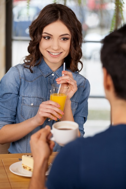 Couple au restaurant. Beau jeune couple assis ensemble au restaurant tandis qu'une femme tenant un verre avec du jus d'orange et souriant