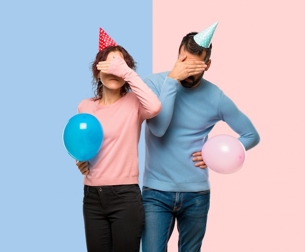 Couple Avec Des Ballons Et Des Chapeaux D'anniversaire Couvrant Les Yeux Par Des Mains