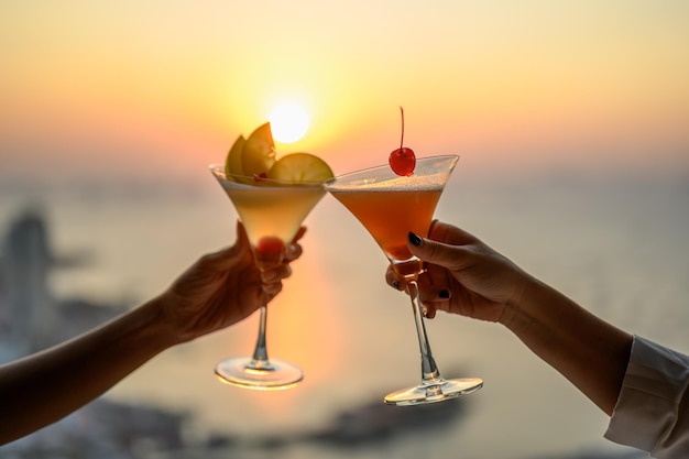Couple bénéficiant d'un verre de cocktail Cheers dans un restaurant au coucher du soleil avec vue sur la mer. Cocktail, Couple, Lune de miel, Dîner, Vin, Concept romantique.