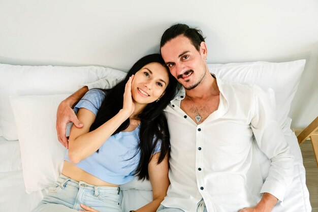 Photo un couple blanc heureux et souriant allongé sur un lit confortable se détendant et se regardant dans les yeux